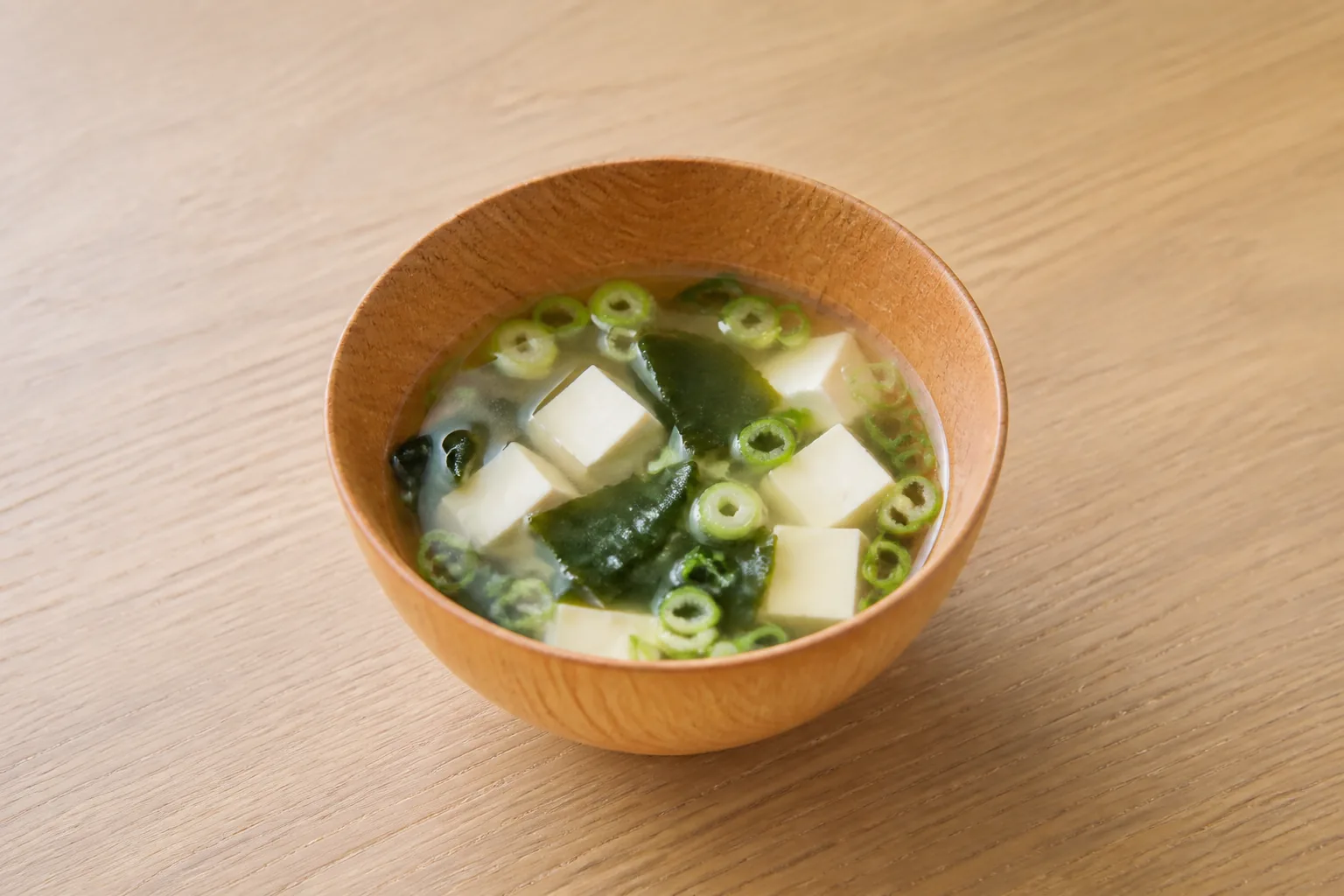 木の器に盛られた汁物。豆腐、わかめ、青ねぎ